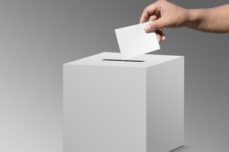 Person wirft einen Zettel in eine Wahlbox
